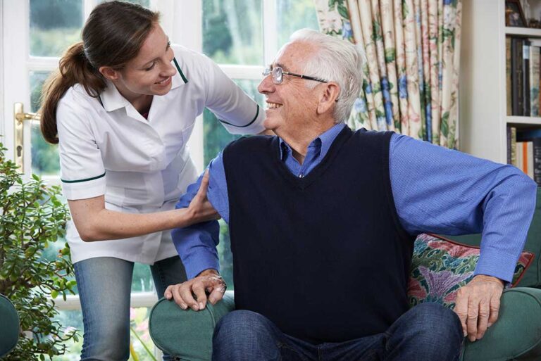 Older adults talking and smiling together at a dining table in a bright, welcoming communal space.