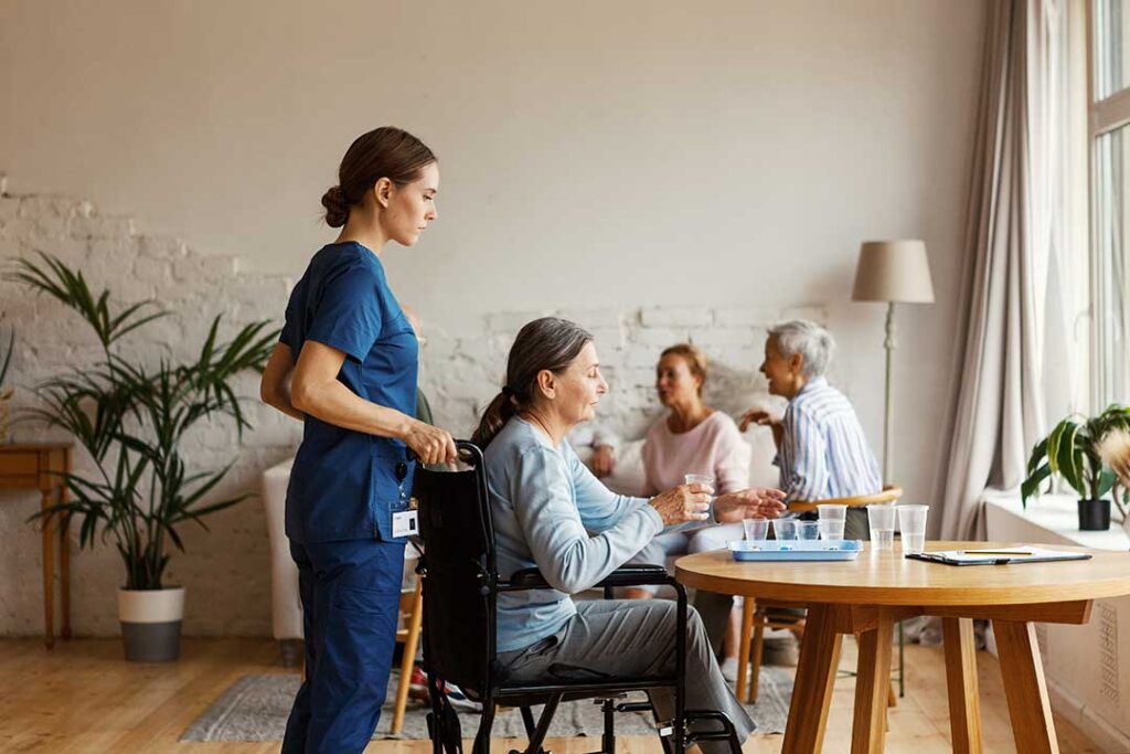 Older adult welcomes family visitors in a bright assisted living lounge with chairs and a sign-in desk.